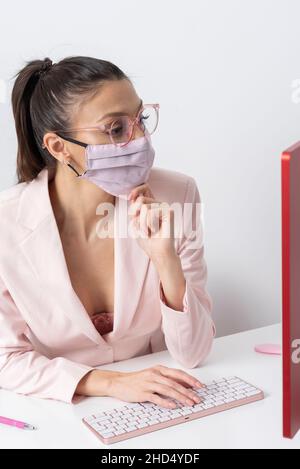 Salisbury, Wiltshire, Großbritannien. 2021. Attraktive Frau trägt rosa Gesichtsmask und mit einem Computer und Tastatur. Stockfoto