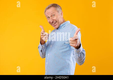 Glücklicher reifer Mann, der im Studio mit den Fingern auf die Kamera zeigt Stockfoto