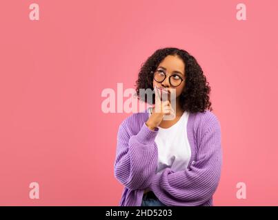 Porträt einer nachdenklichen schwarzen Frau, die das Kinn berührt und auf den Kopierbereich auf pinkem Studiohintergrund schaut Stockfoto