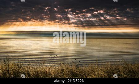 Die Sonnenstrahlen bilden sich durch Wolken über einer ruhigen Nordsee. Stockfoto
