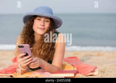 Junge Frau am Strand auf einem Handtuch mit dem Handy. Stockfoto