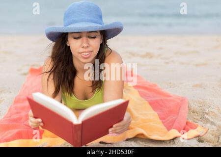 Junge Frau am Strand auf einem Handtuch beim Lesen eines Buches Stockfoto