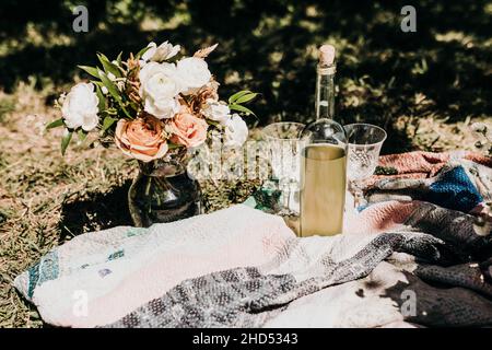 Frisch geschnittene Blumen in einer Vase beim Picknick mit Gläsern und Wein Stockfoto