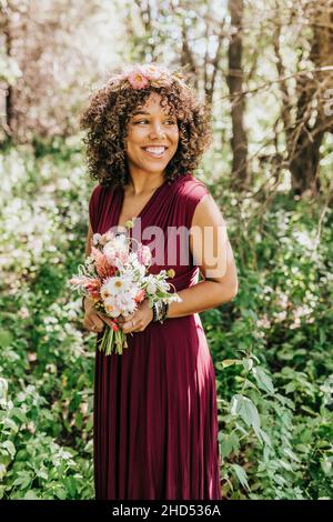 Frau, die im Wald mit frischen Blumen und floraler Krone steht Stockfoto