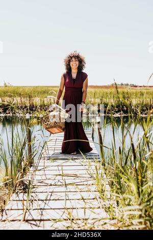 Frau geht auf dem Dock, während sie einen Korb voller Blumen hält Stockfoto