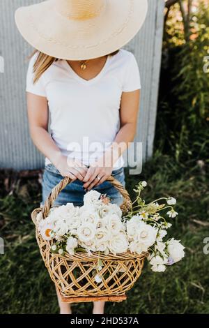 Die Frau hält einen Korb voller frischer Rosen und wilder Blumen Stockfoto