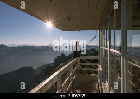 Frau, die bei Sonnenaufgang auf dem Mount Pilchuck Feueraussicht sitzt Stockfoto