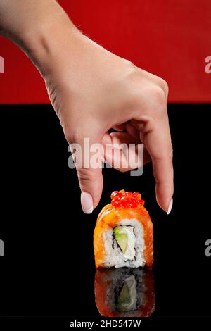 Weibliche Hand, die sich zur Philadelphia Sushi-Rolle mit Lachs streut Stockfoto