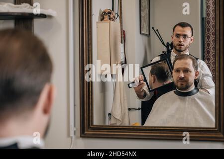 Der Friseur zeigt den Haarschnitt des Kunden von hinten im Spiegelbild. Stockfoto