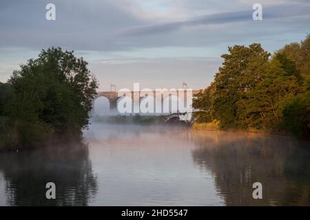 Nebliger Sommersonnenaufgang am Dutton Viadukt, der die Hauptlinie der Westküste über die Weaver-Navigation nördlich der Acton Bridge in der Nähe von Chaeshire führt Stockfoto