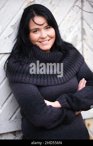 Porträt einer Frau mit gekreuzten Armen vor einer alten Holztür. Stockfoto