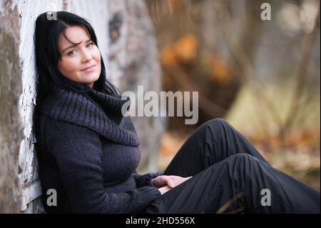 Porträt einer jungen Frau, die auf die Kamera schaut und sich an eine alte Holztür lehnt. Stockfoto