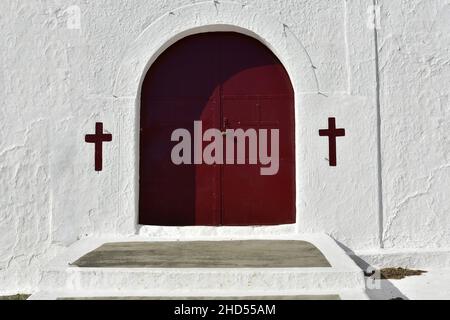 Traditionelles griechisch-orthodoxes Kloster mit gewölbter Holztür mit religiösen Symbolen auf einer weißgetünchten Wand in Leonidio, Arcadia Peloponnes, Griechenland. Stockfoto