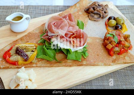 Vorspeise Crepe oder Crepe Antipasto mit Aufschnitt und Vielfalt Von sautenem Gemüse serviert auf hölzernen Brotbrett Stockfoto