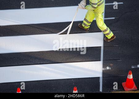 Arbeiter, der Klebeband entfernt hat, nachdem er einen Zebrastreifen auf einer Stadtstraße gemalt hat Stockfoto