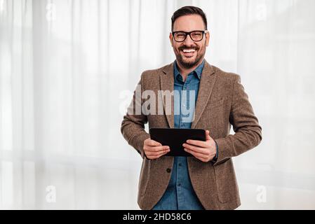 Junge Erwachsene lächelnd fröhlichen Mann Geschäftsmann Unternehmer stehen vor grauem Hintergrund Hintergrund Hand hält Tablet tragbare persönliche Informationen Stockfoto