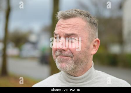 Mann, der mit einem angstvollen Gesichtsausdruck beiseite schaut, der seine Augen mit einem aufgewühlten Stirnrunzeln aus der Nähe schielt Stockfoto