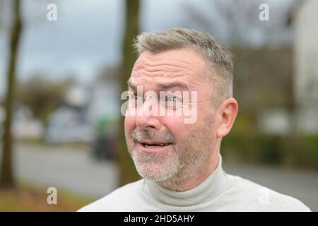 Verstörter Mann mittleren Alters, der draußen auf der Straße steht und mit einem verängstigenden Ausdruck zur Seite schaut Stockfoto