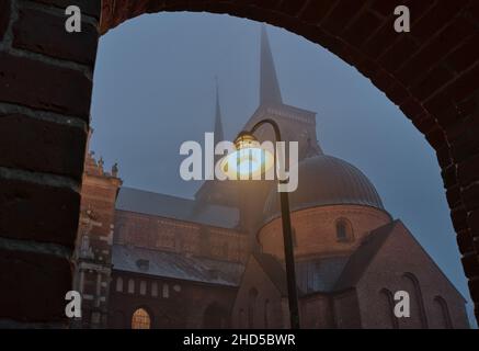 kathedrale von roskilde, durch einen Bogen gesehen, beleuchtet von einer Straßenlampe im Nebel, Roskilde, Dänemark, 1. Januar 2022 Stockfoto