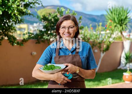 Porträt einer Frau mittleren Alters im Garten mit Schale frischer Minze Stockfoto
