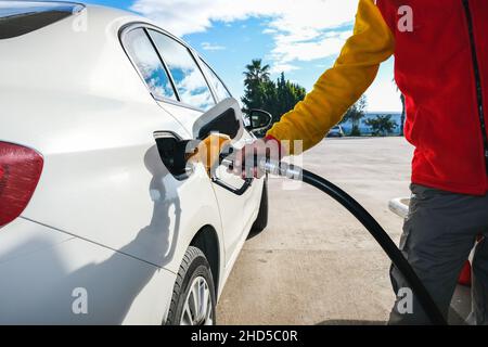 Der Mensch pumpt Benzin im Auto an der Tankstelle und wird in der Tankstelle einen Tank mit weißem Auto füllen, Konzept des globalen fossilen Kraftstoffverbrauchs. Stockfoto