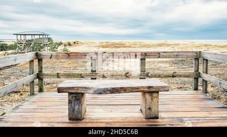 Eine Holzbank mit Blick auf die Sanddünen der Kurischen Lagune und der Kurischen Bucht Stockfoto