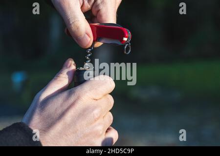 Öffnen einer Weinflasche mit einem Taschenmesser Korkenzieher. Nahaufnahme bei Sonnenuntergang Stockfoto