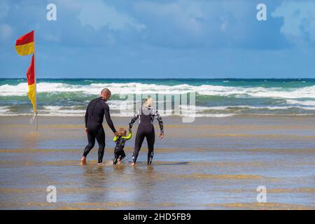 Eine Mutter und ein Vater halten die Hände mit ihrem Kleinkind, das im Meer bei Mawgan Porth in Cornwall paddelt. Stockfoto