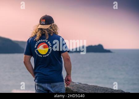 Abendlicht über einem Mann mit einem unverwechselbaren T-Shirt und Blick auf die Fistral Bay in Newquay in Cornwall. Stockfoto