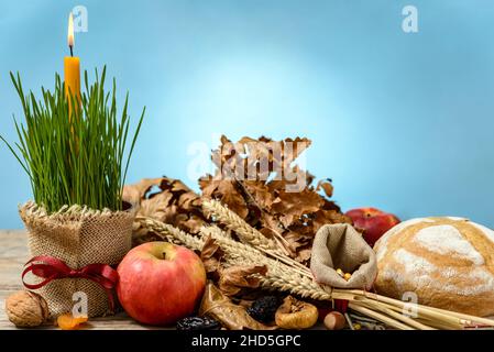 Traditionelles Essen für den orthodoxen Heiligabend. Yule log oder badnjak, die Äpfel, das Brot, die Getreide, die getrockneten Früchte und die brennende Kerze im grünen Weizen auf dem Holz Stockfoto