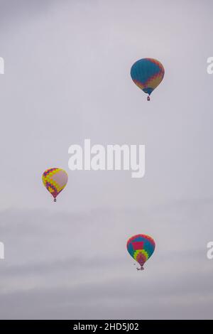 Drei Heißluftballons fliegen beim Winter Aerostat Festival gegen den grauen Himmel Stockfoto