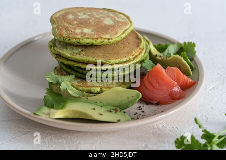 Spinatpfannkuchen mit Avocado und gesalzenem Lachs auf hellem Hintergrund aus nächster Nähe, gesundes Frühstück oder Brunch Stockfoto