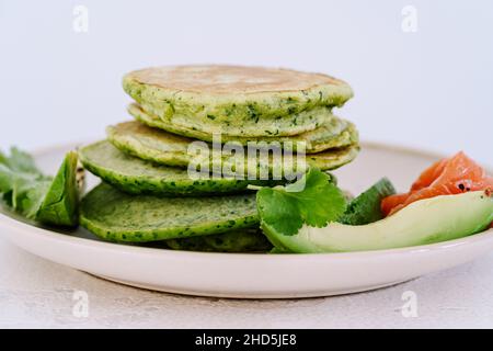 Spinatpfannkuchen mit Avocado und gesalzenem Lachs auf hellem Hintergrund aus nächster Nähe, gesundes Frühstück oder Brunch Stockfoto