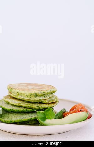 Spinatpfannkuchen mit Avocado und gesalzenem Lachs auf hellem Hintergrund aus nächster Nähe, gesundes Frühstück oder Brunch Stockfoto