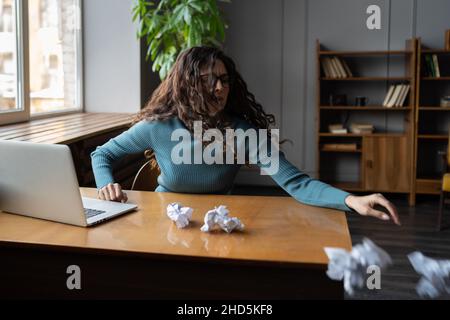 Gestresste hysterische junge Frau, die zerknittertes Papier warf und bei der Arbeit Nervenzusammenbruch hatte Stockfoto