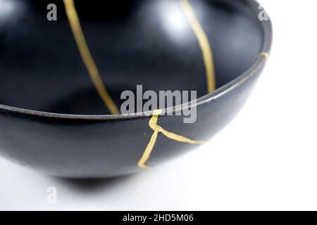 Kintsugi Gold Risse Restaurierung, japanische schwarze Schale mit der antiken Kintsukuroi Restaurierung Technik, die Schönheit der Unvollkommenheiten, fixiert, darstellen Stockfoto