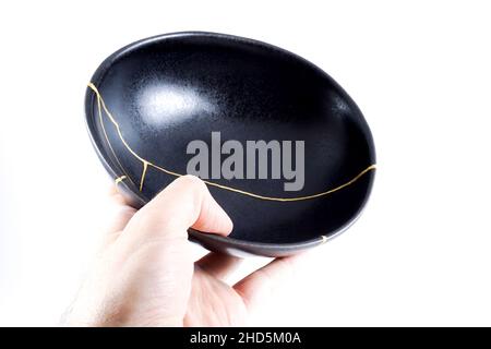 Kintsugi Gold Risse Restaurierung, japanische schwarze Schale mit der antiken Kintsukuroi Restaurierung Technik, die Schönheit der Unvollkommenheiten, fixiert, darstellen Stockfoto