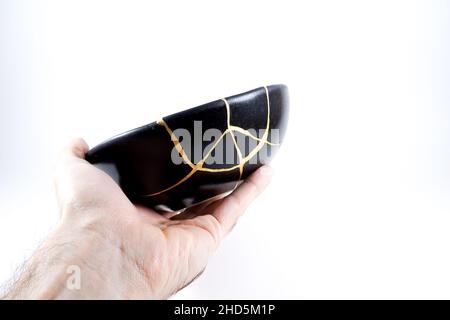 Kintsugi Gold Risse Restaurierung, japanische schwarze Schale mit der antiken Kintsukuroi Restaurierung Technik, die Schönheit der Unvollkommenheiten, fixiert, darstellen Stockfoto