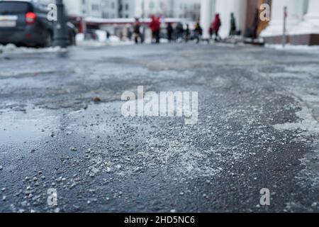 Enteisungsreagenz im Winter auf der Straße. Der Bürgersteig ist mit technischem Salz bestreut Stockfoto