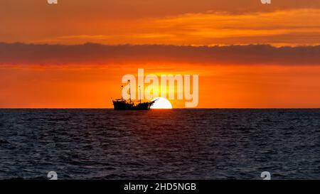 Ein Piratenschiff sitzt auf dem Ozean, der gegen EINEN SILHOUETTIERT ist Farbenprächtiger Orangefarbener Sonnenuntergang Am Himmel Stockfoto