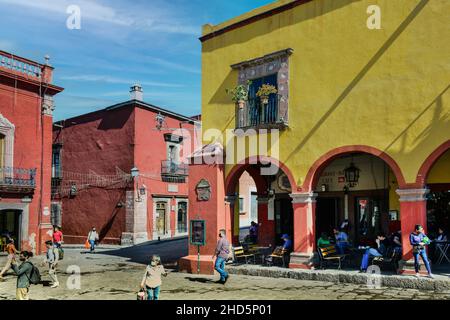 Alte Gebäude aus der spanischen Kolonialzeit und Menschen, die am El Jardin Platz arbeiten, genießen das Café-Leben und Einkaufen in El Centro in San Miguel de Allende, MX Stockfoto