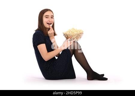 Mädchen, das mit einer Schüssel Popcorn auf dem Boden sitzt. Isoliert auf Weiß. Hochauflösendes Foto. Stockfoto