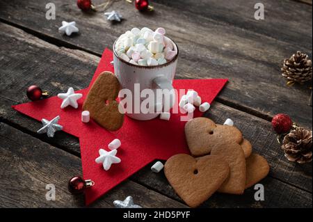 Wunderschöne Urlaubsumgebung mit riesigen herzförmigen Plätzchen, einer Tasse köstlicher heißer Schokolade mit winzigen Marschmalchen und weihnachtsdekoration auf der R Stockfoto