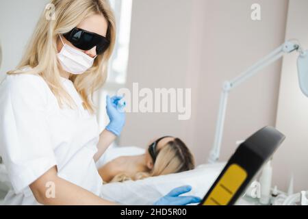Die Laserhaarentfernungsspezialistin in der Schutzbrille bereitet den Epilierer auf den Eingriff vor Stockfoto