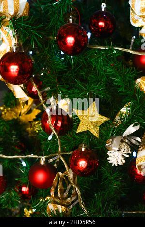 Nahaufnahme eines grünen Weihnachtsbaums mit roten Ornamenten, goldenen Sternen, Lichtern und Bändern im Dezember in den USA Stockfoto