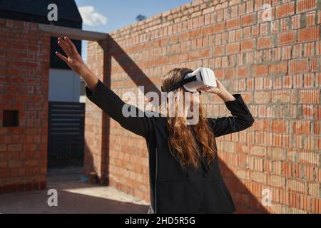 Eine Arbeiterin schaut durch eine VR-Brille und streckt den Arm aus Stockfoto