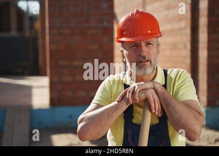 Müder Arbeiter, der mit den Händen auf dem Schaufelgriff ruht Stockfoto