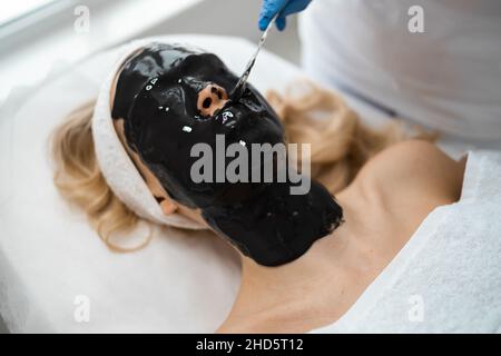 Kosmetologe, der im Schönheitssalon eine Alginatmaske auf das Gesicht einer jungen Frau anwendet. Hautpflege im Schönheitssalon Stockfoto