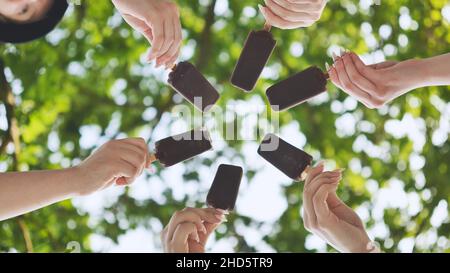 Freunde halten Schokoladeneis auf einem Stock und legen es in einen Kreis. Stockfoto