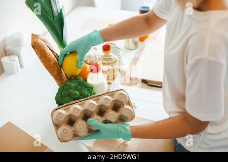 Frau in einem weißen T-Shirt verpackt Lebensmittel in einen Pappsack. Das Konzept der Unterstützung und Freiwilligenarbeit, Spende Stockfoto